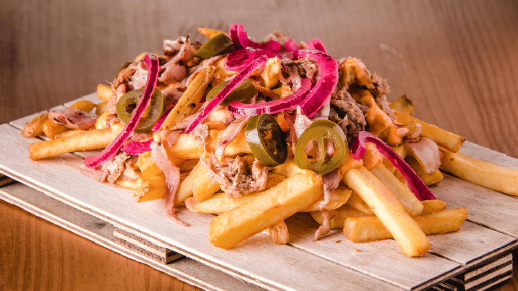 Platter of French fries topped with shredded meat, red onions, and jalapeño peppers