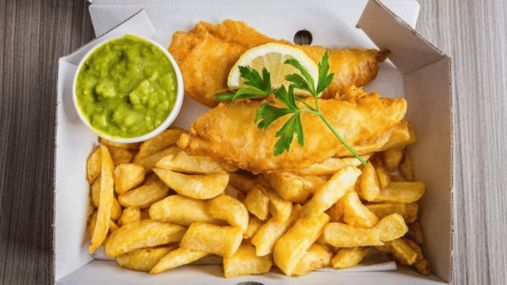 Overview of container of fried fish, French fries and mushy peas in a ramekin. 