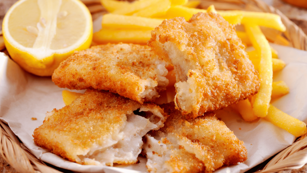 Fish and french fries on white plate with half of lemon next to them. 