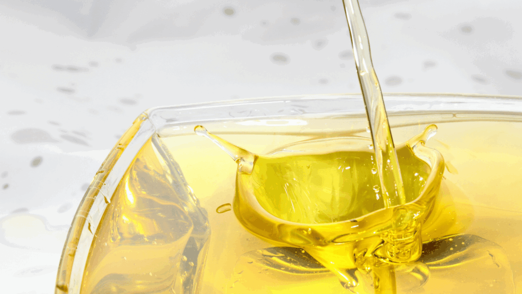 Gold oil in a clear container splashes up as more oil is poured into the container.